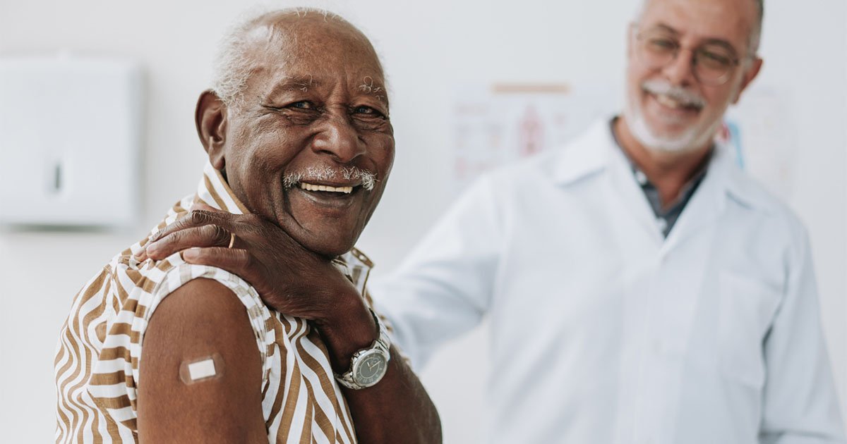 Senior man with band aid on upper arm, doctor in background