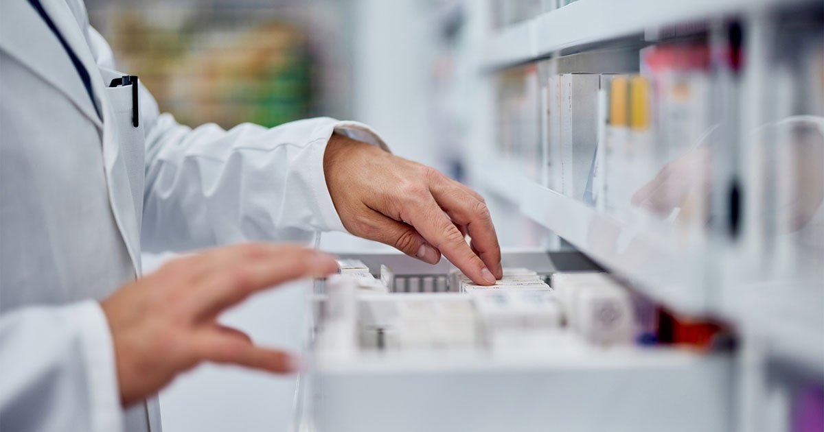 a pharmacist uses his hands to select a medicine from a drawer