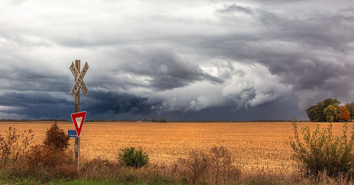 Dramatic sky with dark clouds over a rural railroad crossing with farm field in background