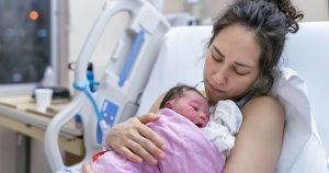 Woman in a hospital bed holds a newborn baby that is wrapped in a pink blanket