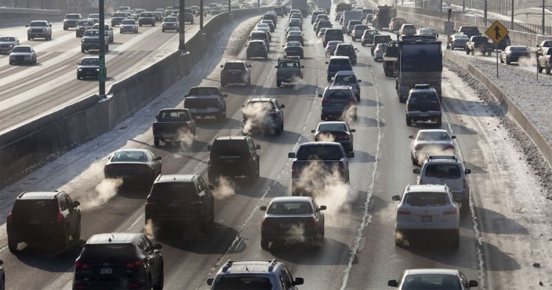 multiple lanes of traffic driving on a highway during winter, exhaust visible from the vehicle's tailpipes