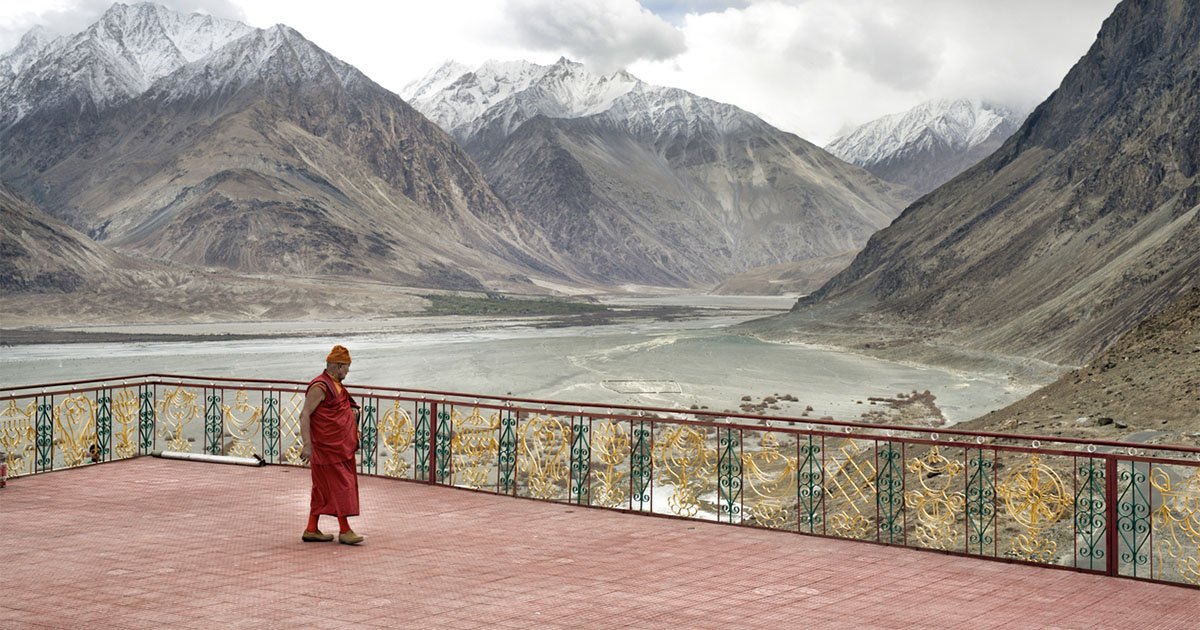 A monk wearing orange robe walking on a deck with the Himalaya mountains in the background