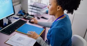 Black woman healthcare worker in a blue uniform working on a computer