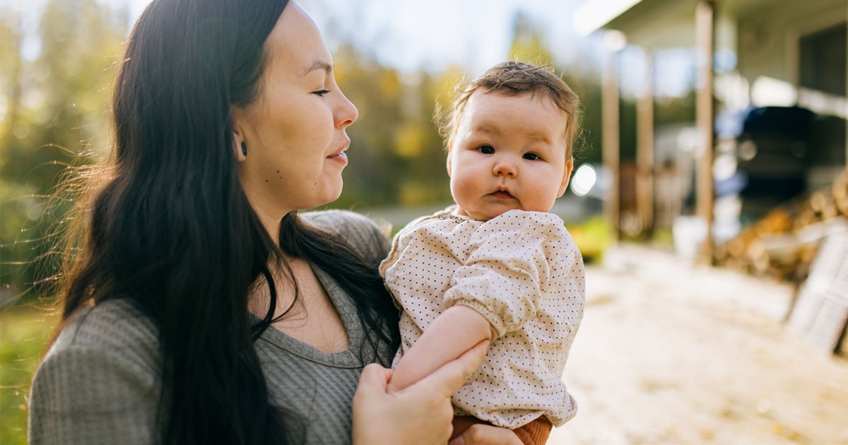 Indigenous American woman holds a baby while standing outside